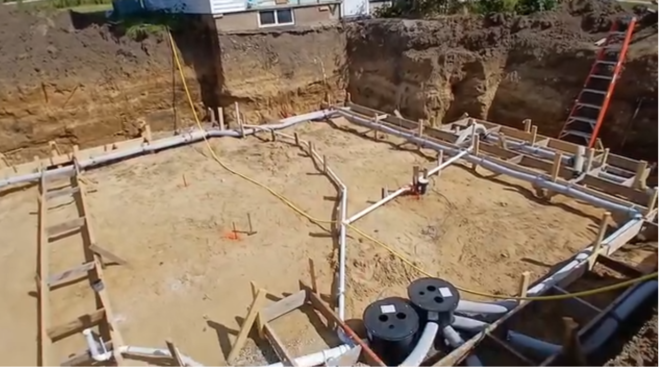 Basement excavation showing concrete spread footing forms, underground plumbing pipes, sump and sewage ejector basins before foundation construction in Cedar Rapids, Iowa.
