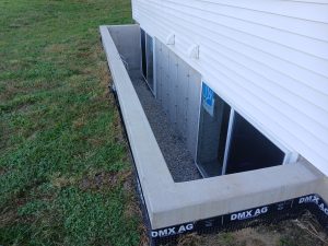 Poured concrete basement window well with reinforced retaining walls, two basement windows and clean drainage stone by Madison's Homes in Iowa
